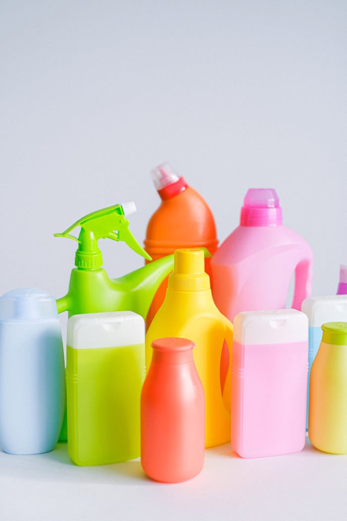 Composition of different colorful plastic containers with detergents for disinfect and daily routine placed on table against white background in room