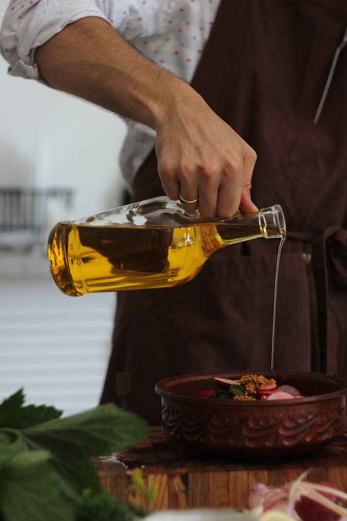 Man pouring olive oil over fresh ingredients in a rustic indoor kitchen.