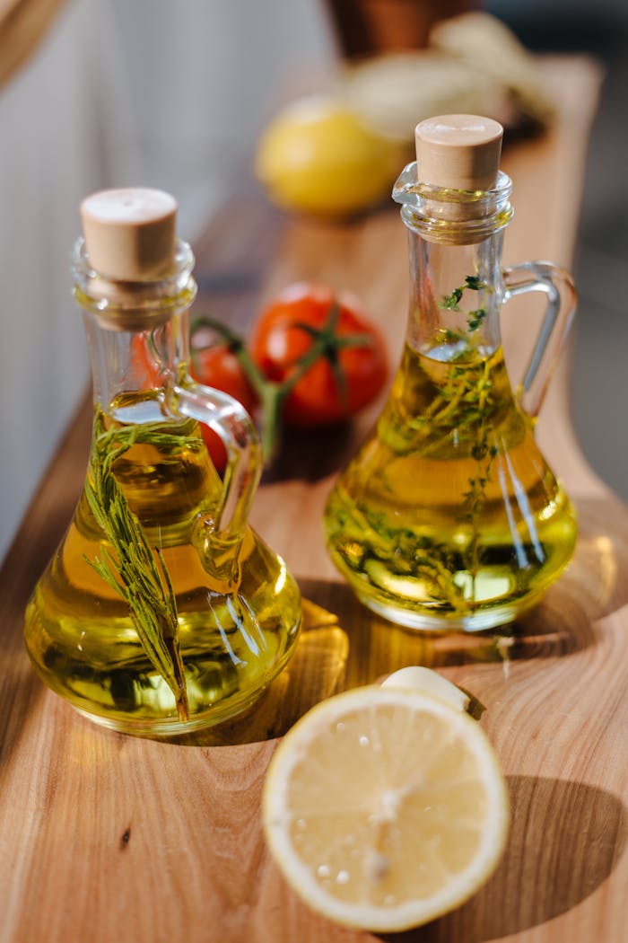 Close-up of herb-infused olive oil with fresh lemon and tomatoes on wooden surface.